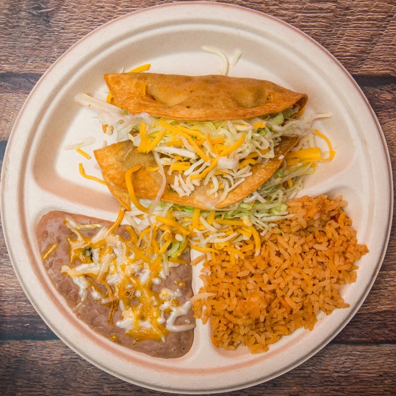 Two crispy tacos with shredded lettuce and cheese, served with refried beans and Mexican rice.